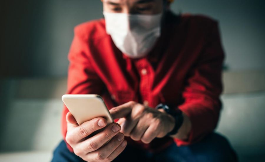 Photo of a man wearing a face mask typing on a mobile phone.